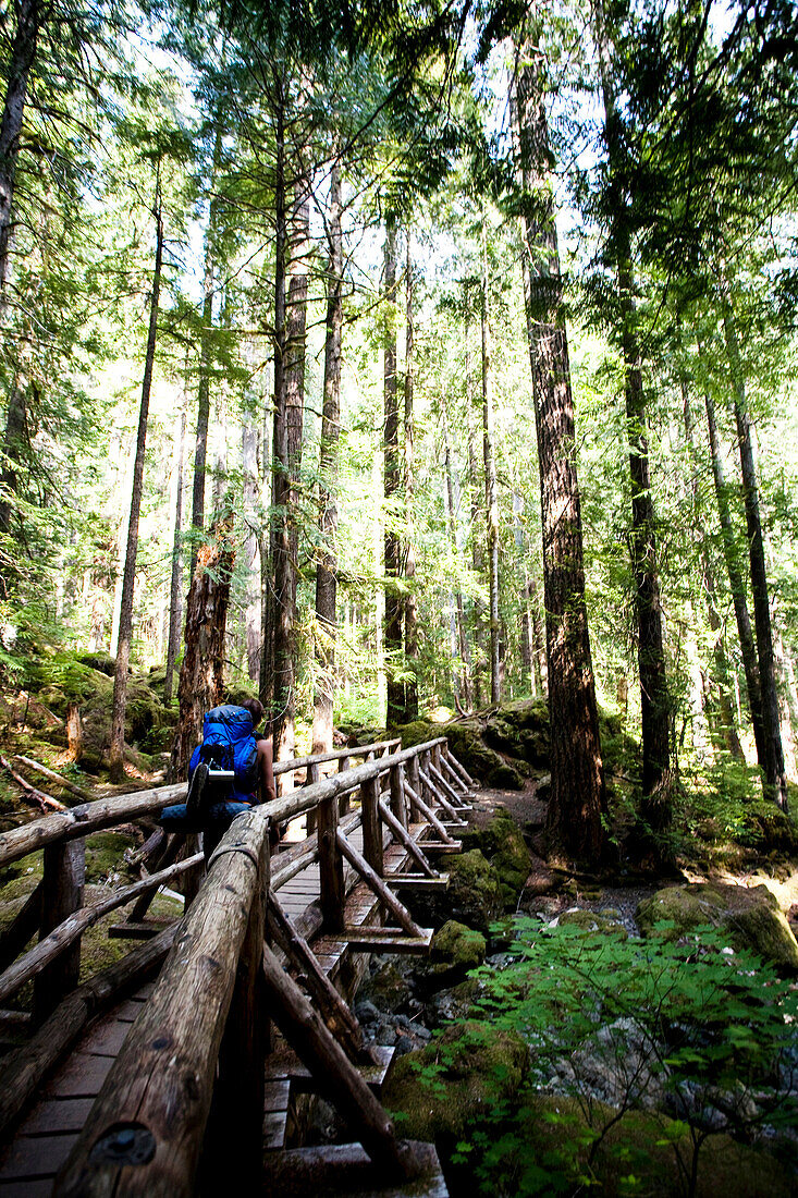 A young girl crosses a wooden bridge while carrying a large backpack, Washington, USA