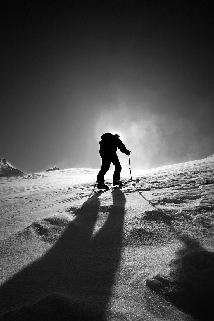 A skier skinning up Mount Baker, Washington with the sun behind him and a shadow cutting across the slope Washington, USA