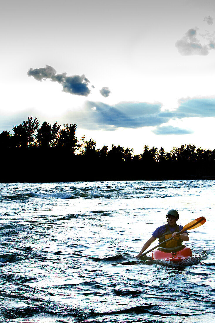 A female kayaker in a playboat paddles out at sunset on the Clark Fork River, Missoula, Montana Missoula, Montana, USA