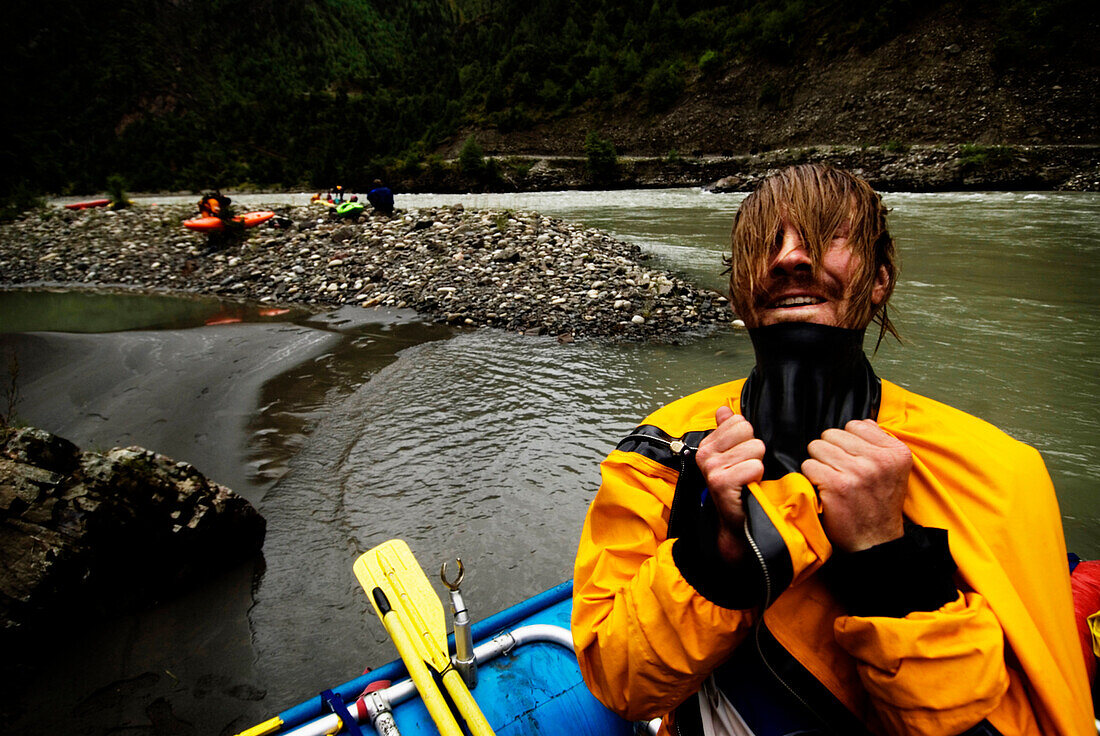 A young male rafter pulls his head through the gasket on his drysuit during a whitewater rafting trip in Western China China