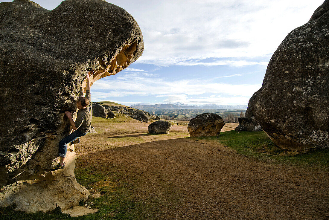 A young man climbs a boulder at Elephant Rocks, New Zealand Elephant Rock, New Zealand