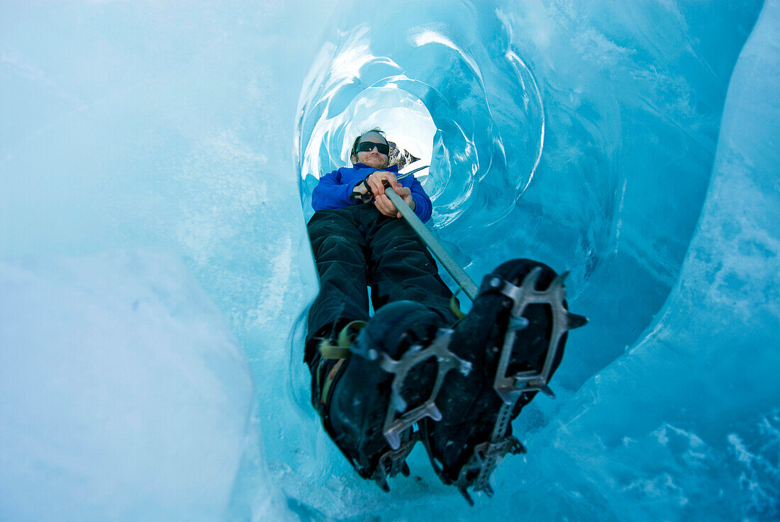 A young man slides down an ice tunnel holding an ice axe in Franz Josef, New Zealand Franz Josef, New Zealand