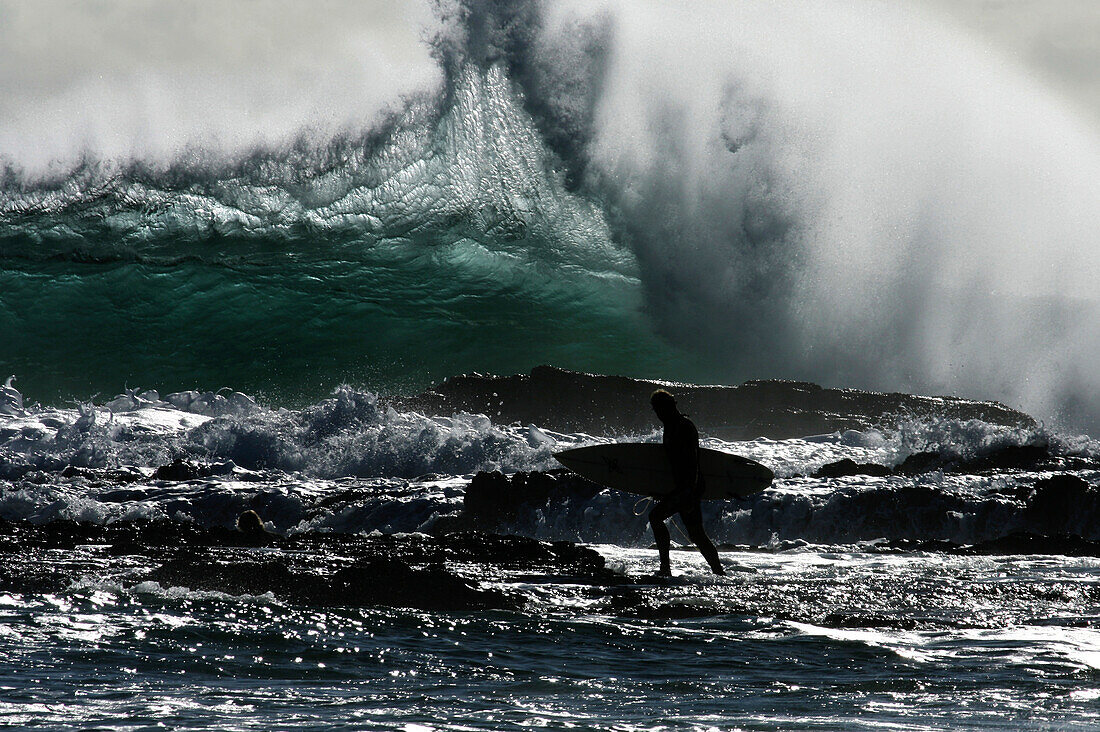 A surfer navigates their way through the rocks on the Gold Coast, Queensland, Australia Gold Coast, Queensland, Australia