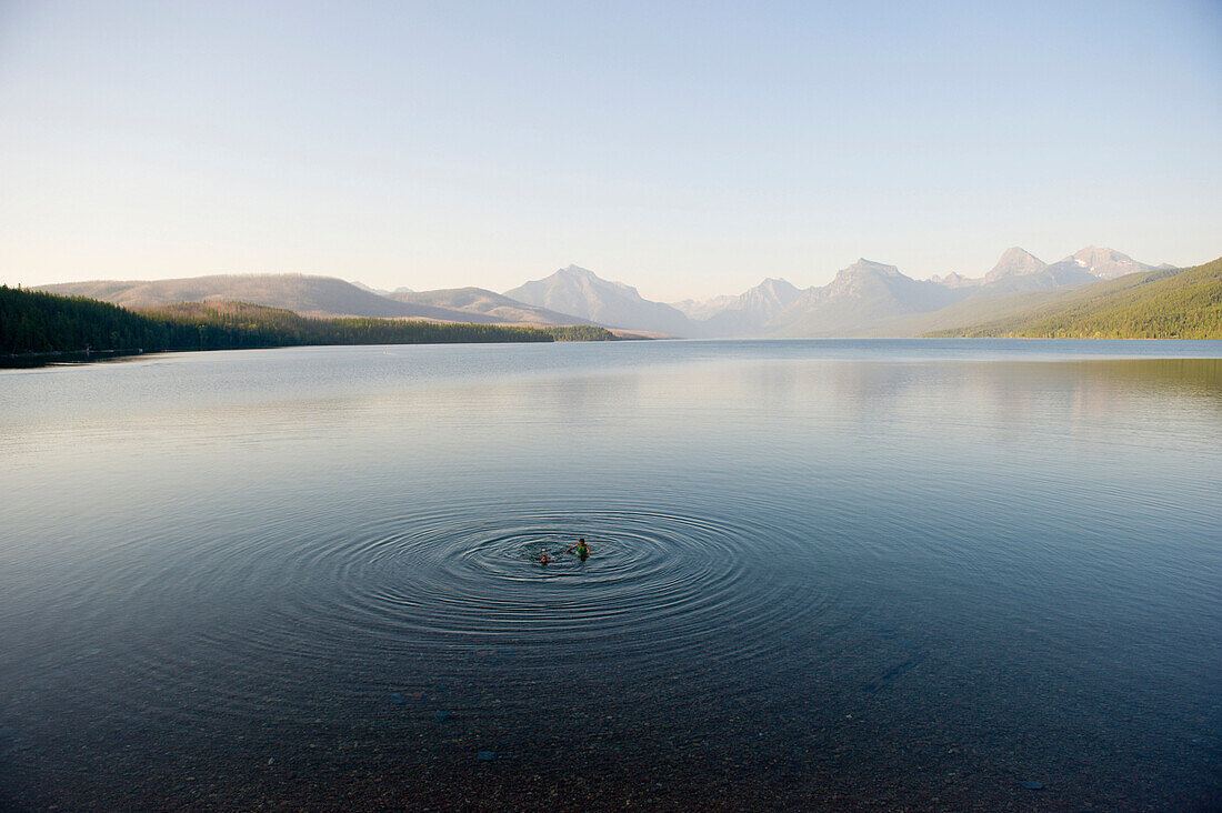 Two young girls take an evening swim in a calm mountain lake in Glacier National Park, Montana Montana, USA