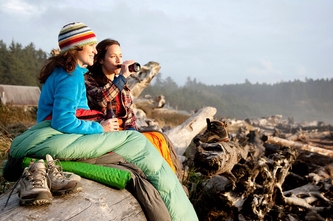 Two beautiful women and drink a beer while enjoying the sunset at La Push Beach, from a drift log La Push, Washington, USA