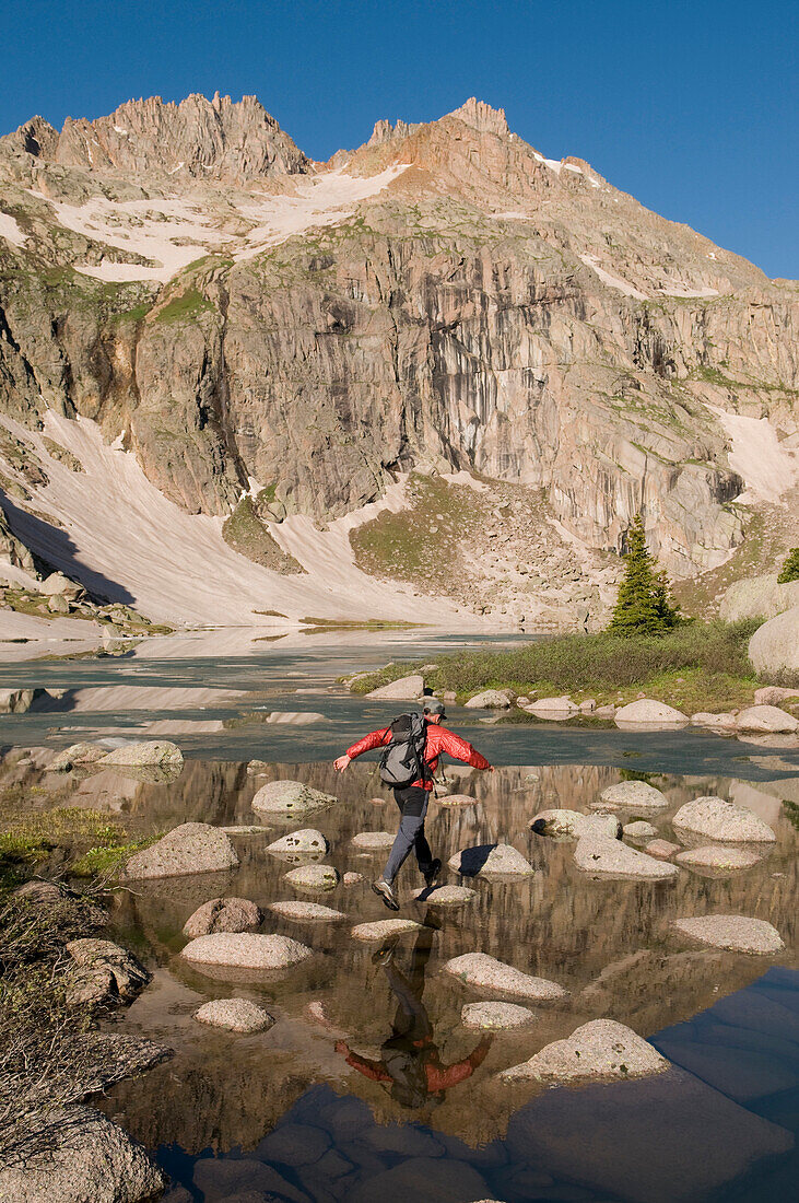 A man jumping across rocks over a lake in the Weminuche Wilderness, San Juan National Forest, Colorado Durango, Colorado, USA