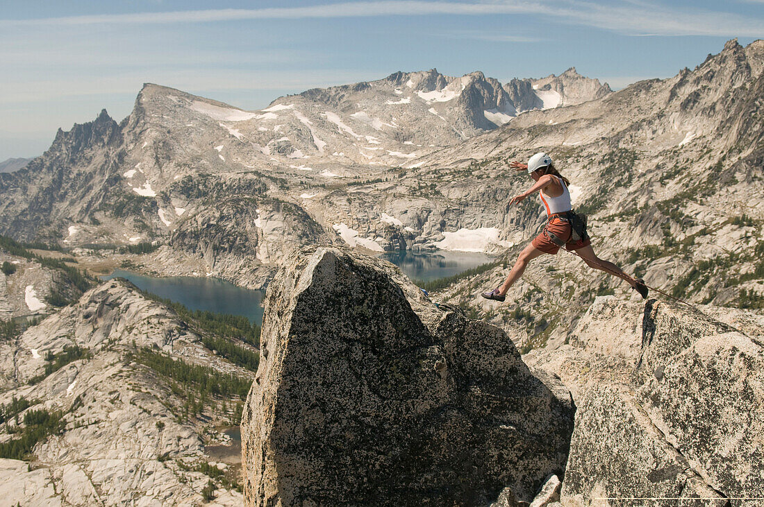 A woman jumping onto a summit in the Enchantment Peaks, Alpine Lakes Wilderness, Leavenworth, Washington Leavenworth, Washington, USA