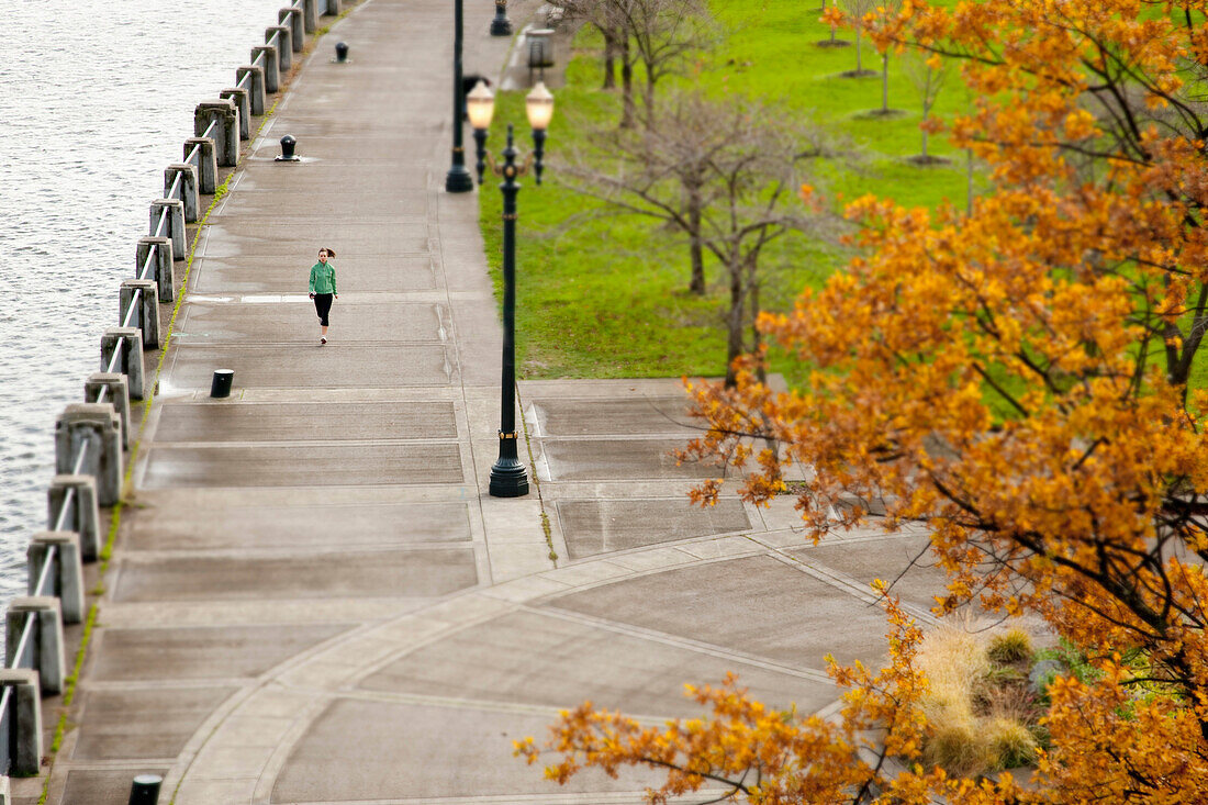 An athletic female in a green jacket jogging along the Portland, Oregon waterfront Portland, Oregon, USA