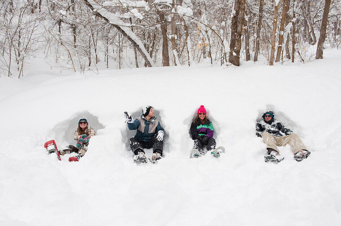 Four young men and women sit in the snow with snowshoes on in Milcreek Canyon, Salt Lake City, Utah Salt Lake City, Utah, USA