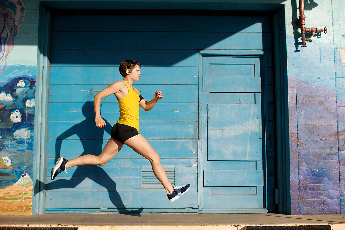 Woman runs and leaps in front of a big blue door in San Diego, California San Diego, California, USA
