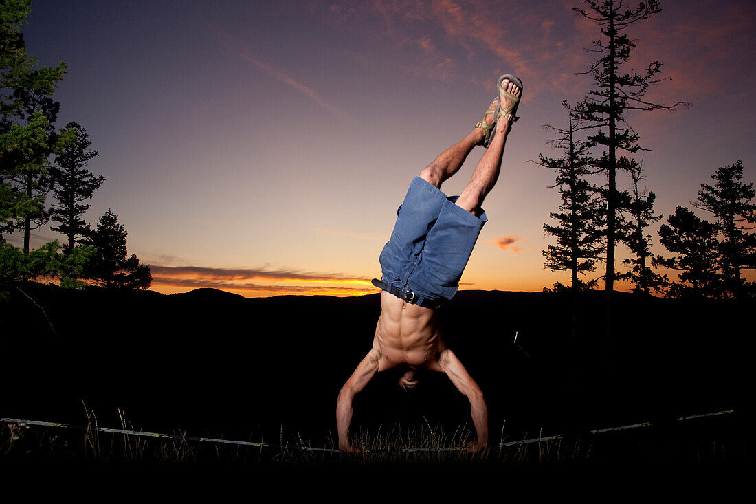 A professional slackliner plays around on the slackline in a field at sunset in the Blue Mountain of Missoula, Montana Missoula, Montana, USA