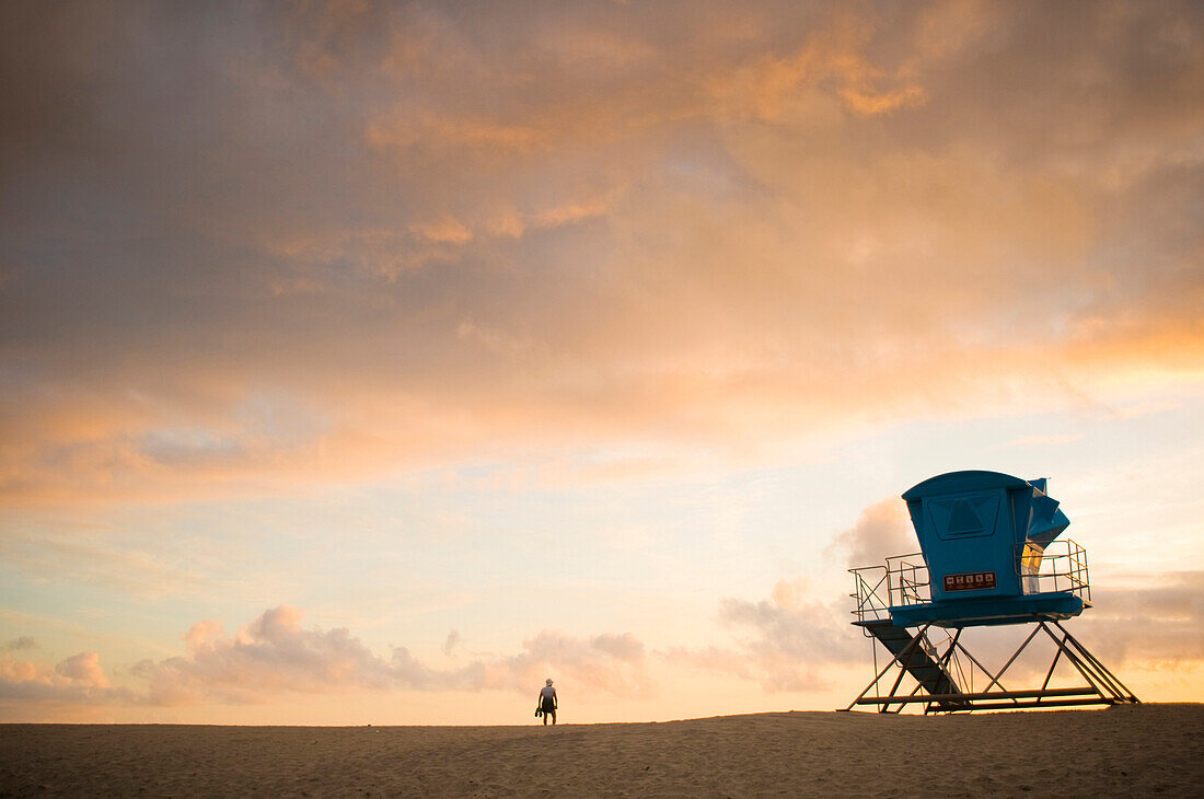 A person next to a life guard tower on the beach watches the sunset San Diego, California, USA