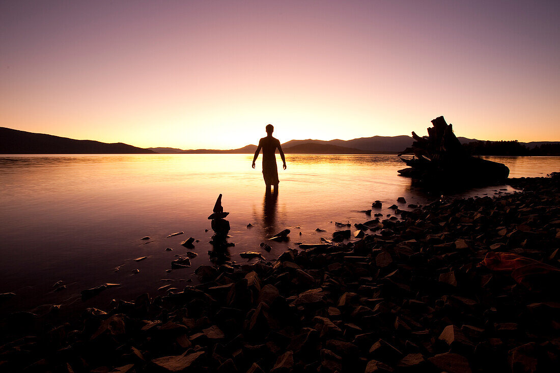 A male figure watching sunset over a lake and mountains in Sandpoint, Idaho Sandpoint, Idaho, USA