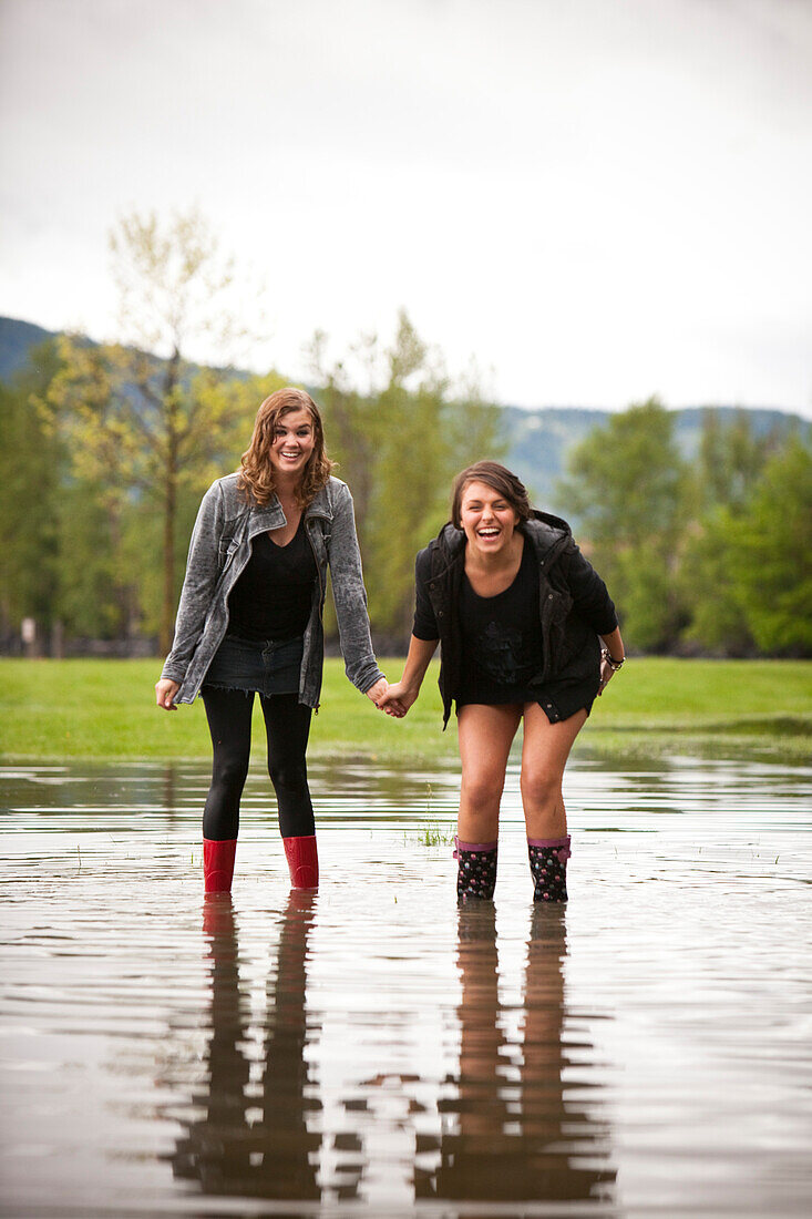 Two young women hold hands after a water fight in a large puddle Sandpoint, Idaho, USA