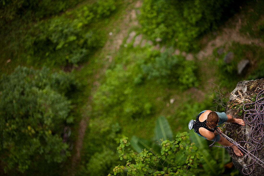 Caucasian female climer looking down from belay station 60 metres above in rural Asia Yangshuo County, Guilin, Guangxi, China