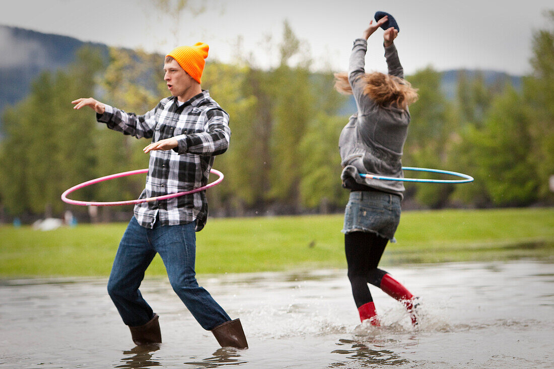 Two young adults dance while hula-hooping in a large puddle Sandpoint, Idaho, USA