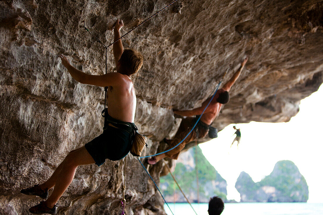 A group of male climbers climbing a severely overhanging wall on the beach in Thailand Hat Tonsai, Krabi, Thailand