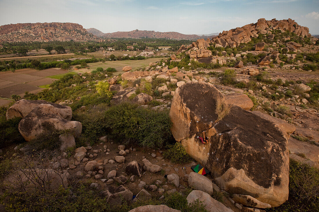 Female climber alone on a massive boulder amid a landscape of stone and brush Hampi, Karnataka, India