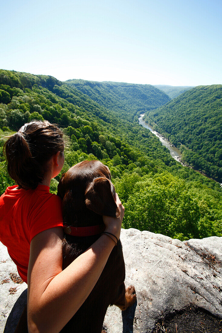 Woman and her dog take in the view from a high mountain cliff Fayetteville, West Virginia, USA