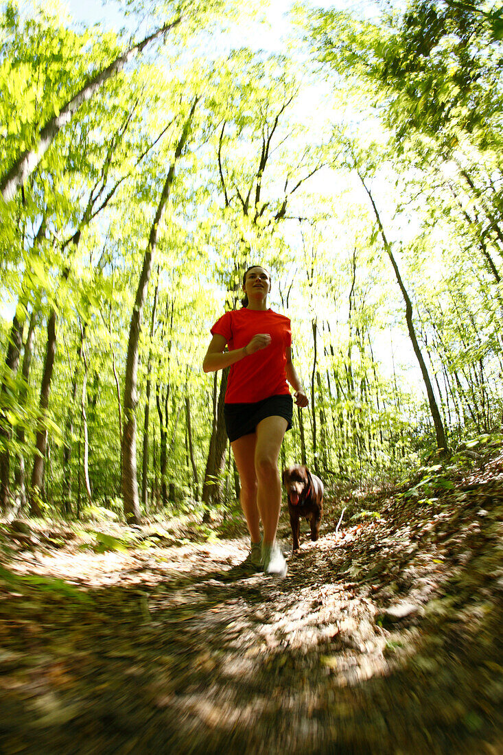 Woman trail running in a lush green forest with her dog Fayetteville, West Virginia, USA