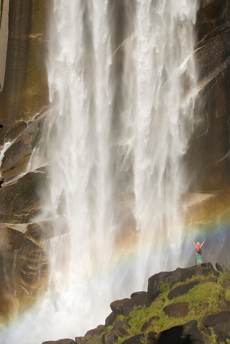 A young woman celebrates under a giant waterfall CA, USA