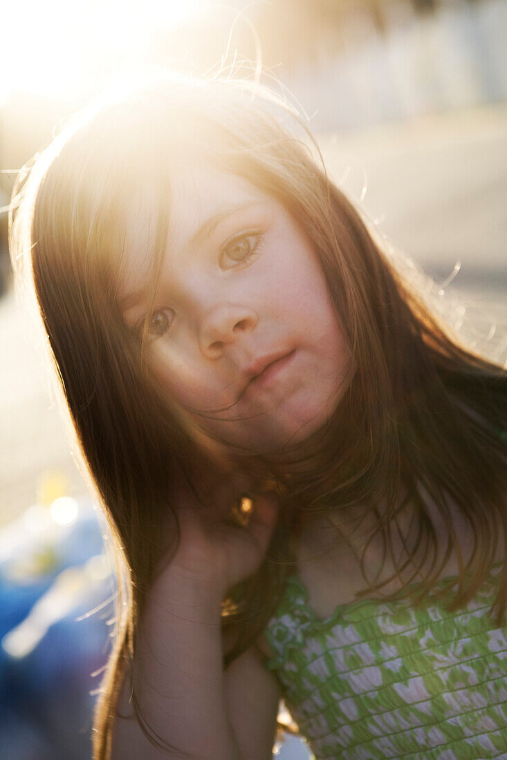 A little girl with long hair is staring at the camera with the sun shining through her hair Destin, Florida, USA