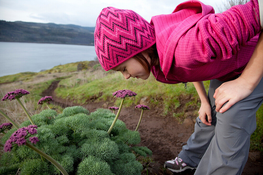 A young girl dressed in pink smells the spring flowers, while out hiking White Salmon, Washington, USA