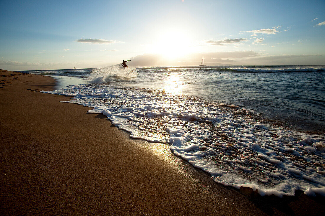One man skimboarding at sunset with sailboats in the background Ka'anapali, Hawaii, USA