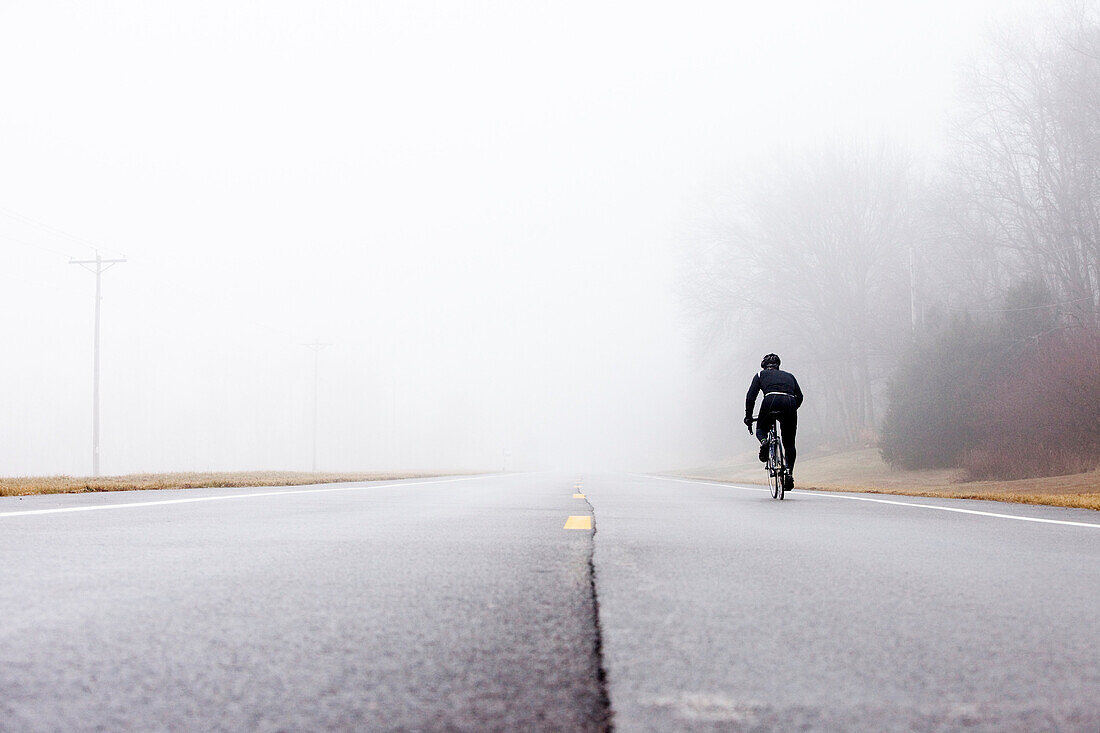 Low angle perspective of one man cycling into a foggy background Ballwin, Missouri, USA