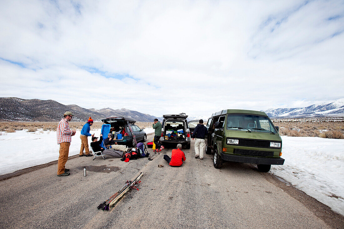Six men hanging out in the middle of a road with their ski gear and vehicles in a remote mountainous area Wendover, Nevada, USA