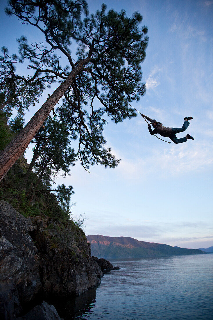 A young adult on a rope swing at sunset in Idaho Sandpoint, Idaho, USA