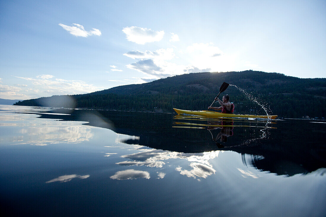 Young man paddles yellow kayak on lake Sandpoint, Idaho, USA