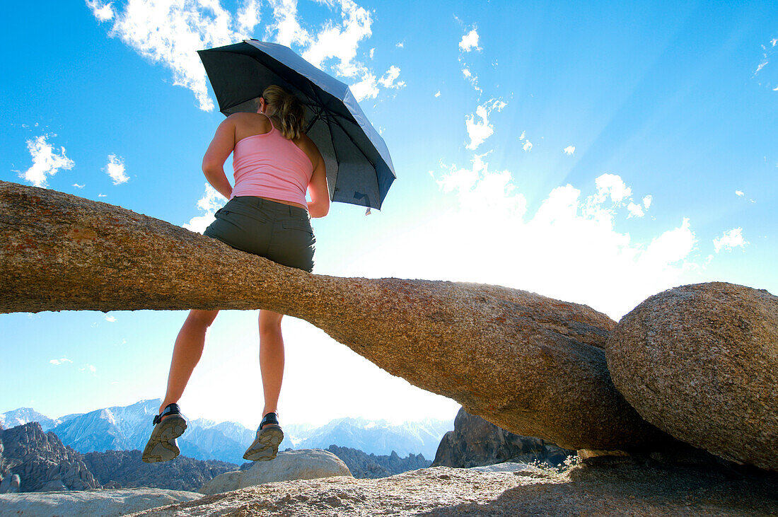 A woman sitting on a natural rock arch holding an umbrella Lone Pine, California, USA