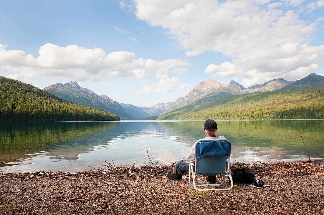 An older man sits next to a lake in Glacier National Park, MT, Montana, USA