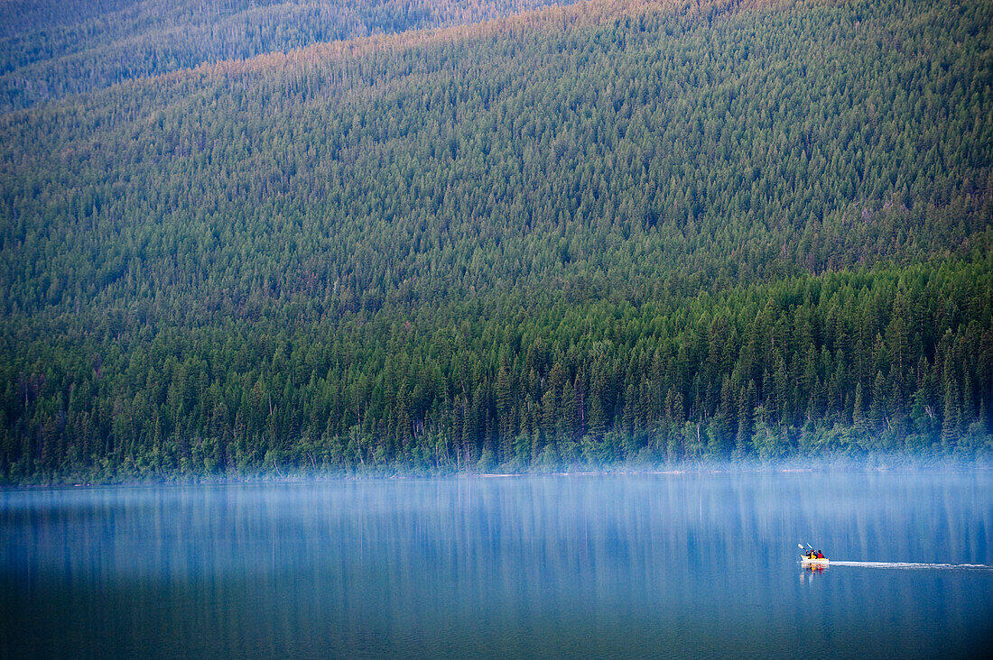 A couple paddles a kayak through a lake in Glacier National Park, MT Montana, USA