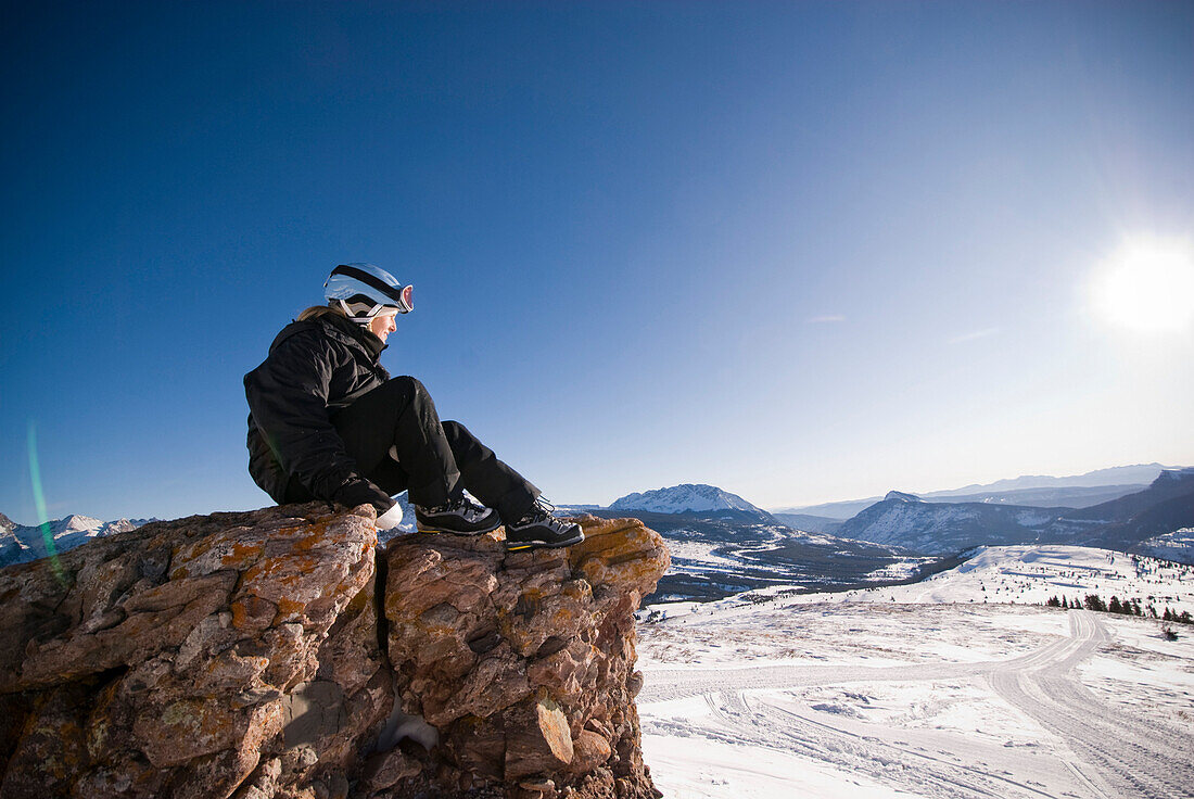A middle aged woman looks into the distance over a valley of snow in the Rocky Mountains Colorado, USA