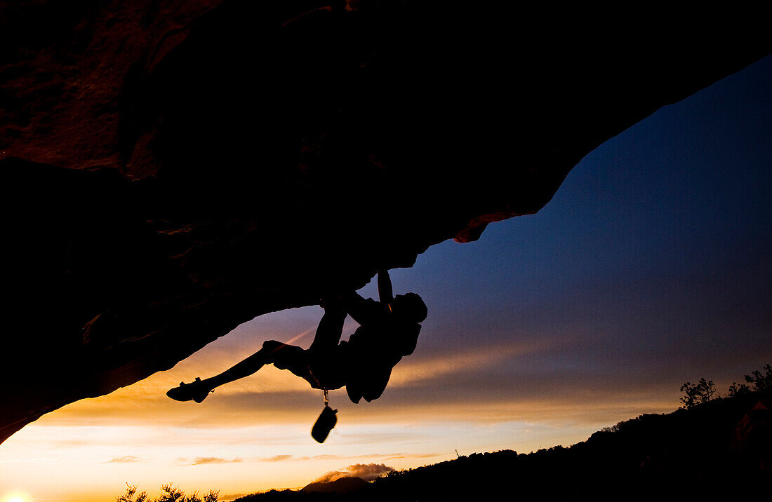 A young man climbs a boulder problem during a sunset overlooking the ocean in Santa Barbara, CA Santa Barbara, California, USA
