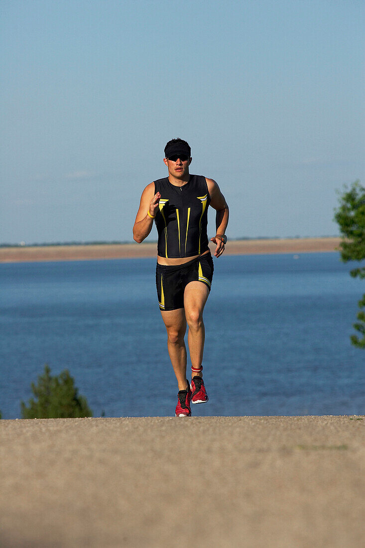 A male athelete running while training for a triathlon at a lake Lawrence, Kansas, USA