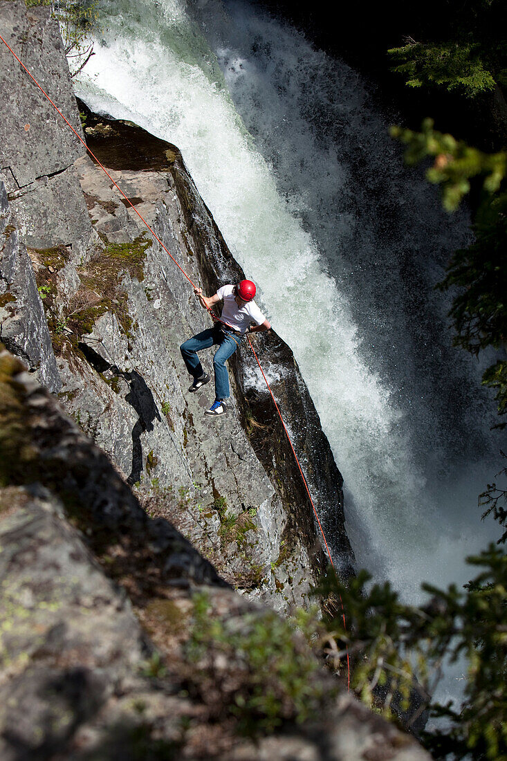 A young man rappels down a cliff next to a waterfall in Idaho Sandpoint, Idaho, USA