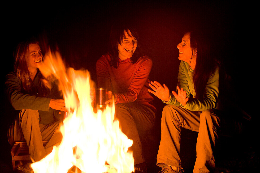 Three women talk and laugh together around a campfire Utah, USA