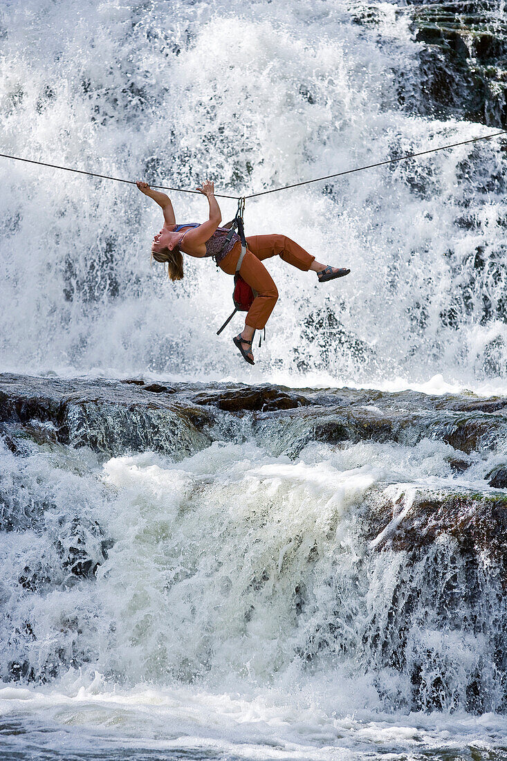 A woman crosses a waterfall using a Tyrolean Traverse on a rope Utah, USA