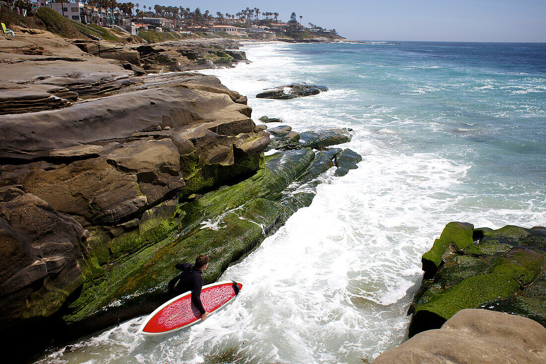 Male surfer in between rocks before jumping in the water to go surfing at Windnsea Beach San Diego, CA, USA