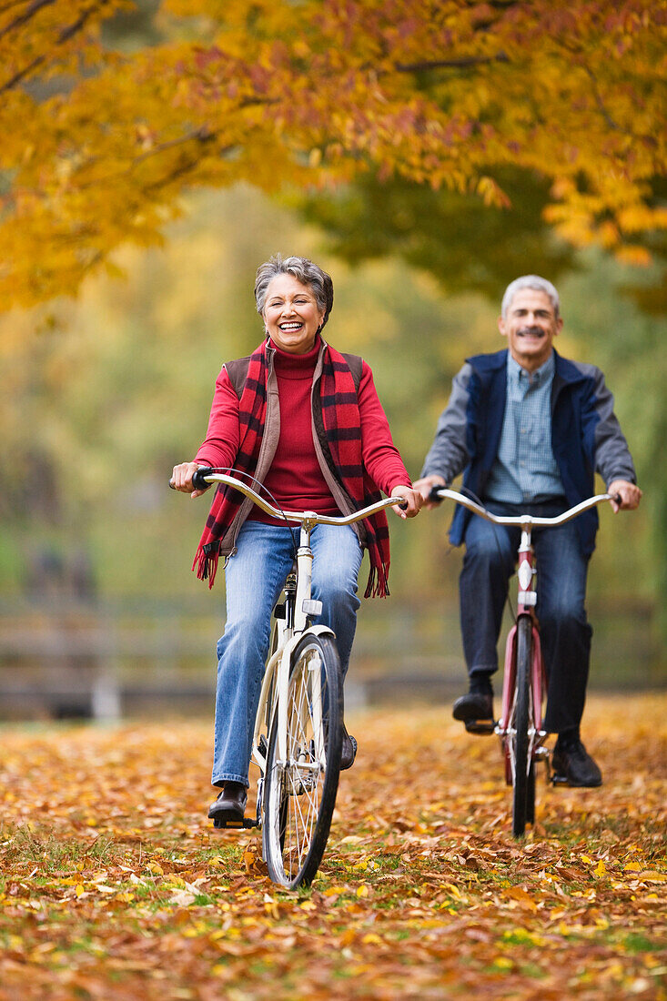 African couple riding bicycles in park in autumn, Seattle, WA