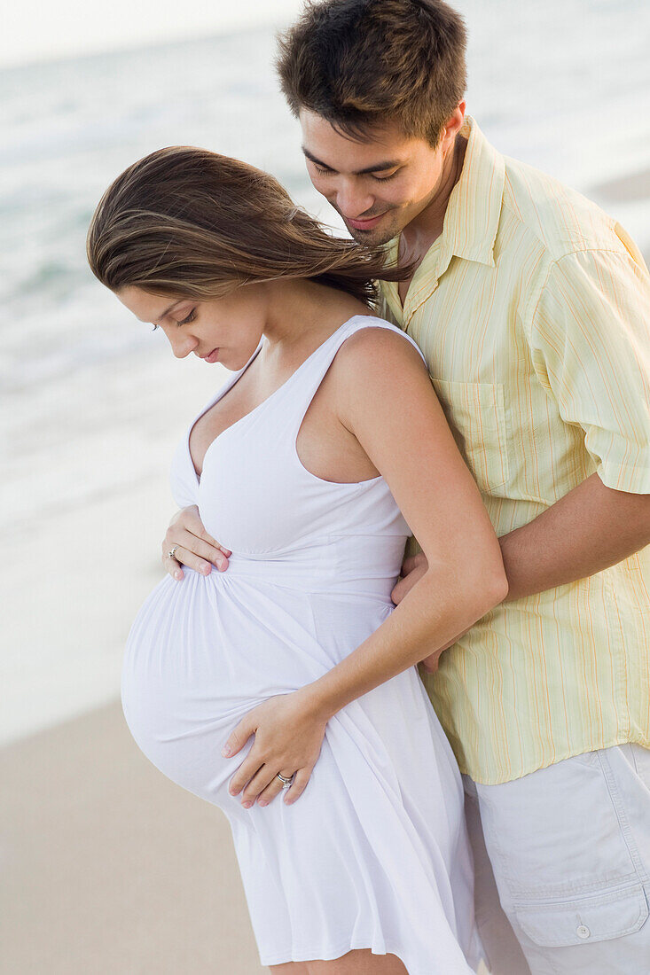 Husband hugging pregnant wife on beach, Fort Lauderdale, FL