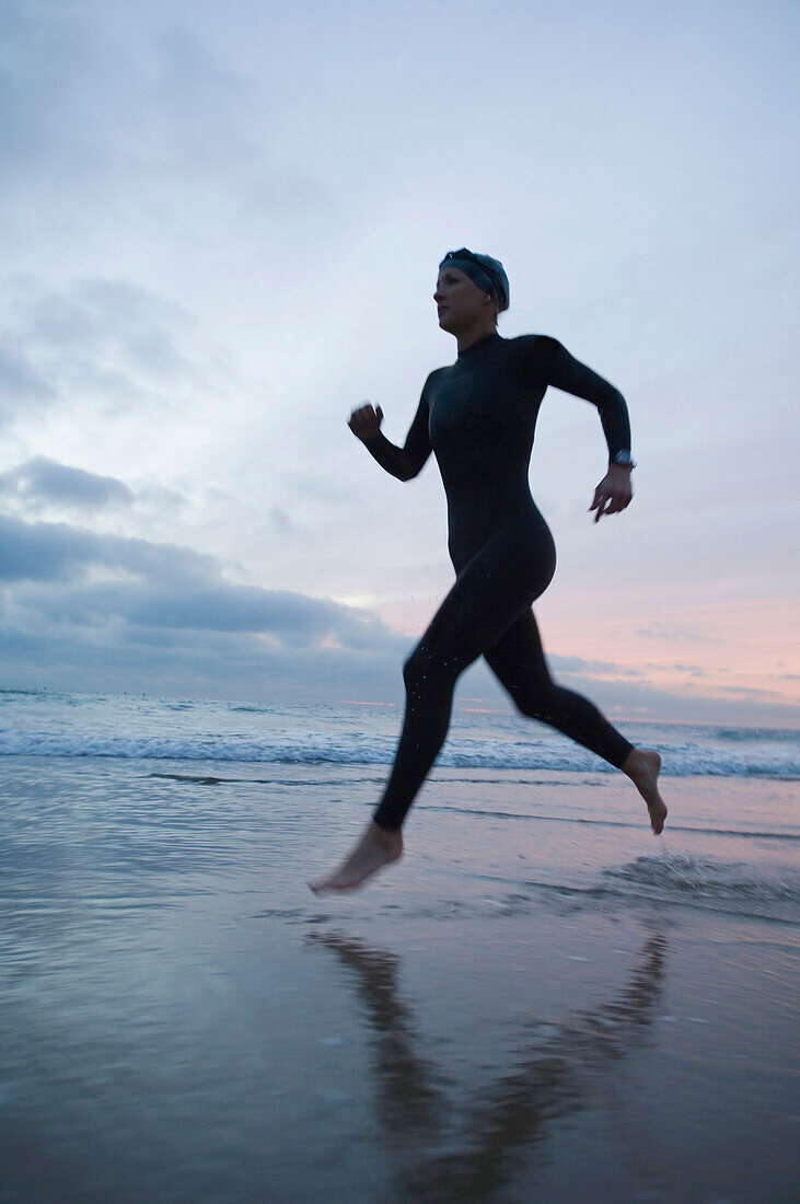 Hispanic woman in wetsuit running on beach, Newport Beach, CA