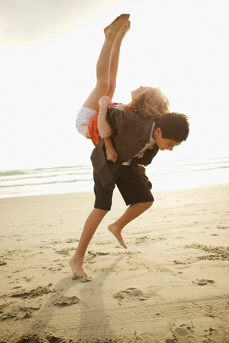 Boy lifting girl on back on beach, Coronado, CA