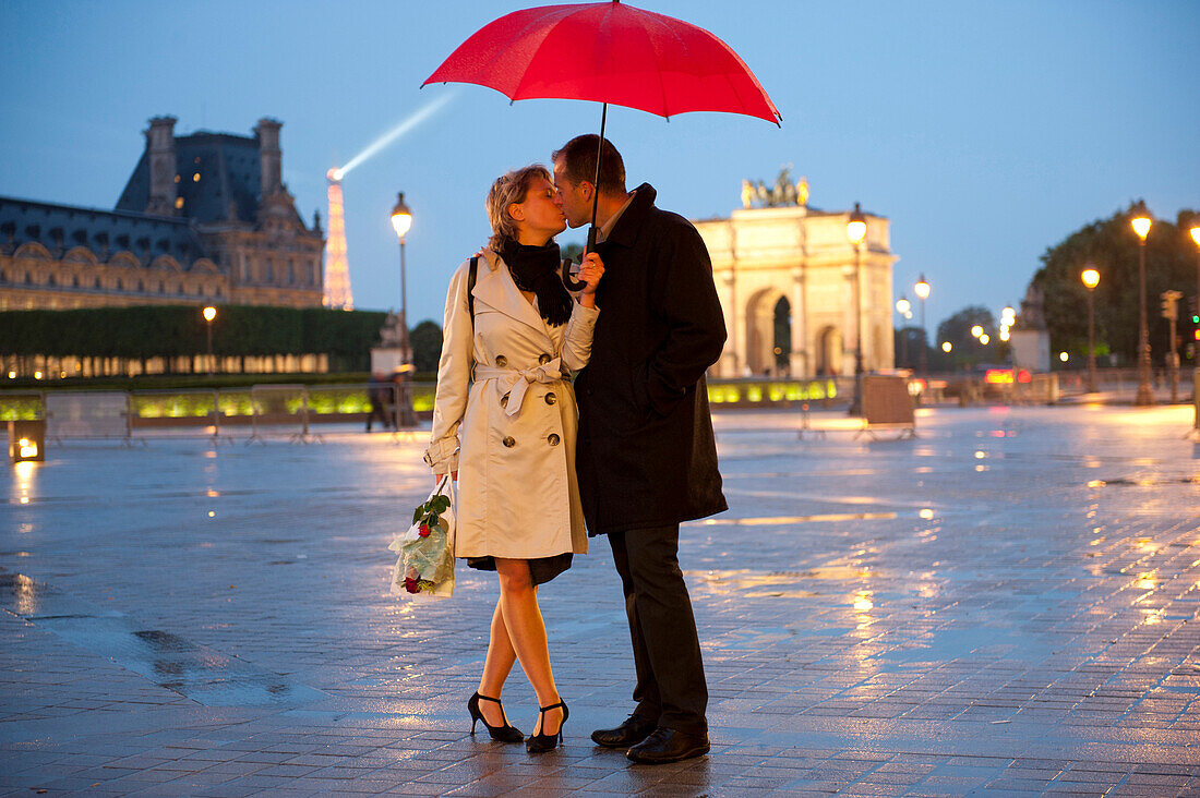 Caucasian couple kissing in rain at night near the Louvre, Paris, Paris, France