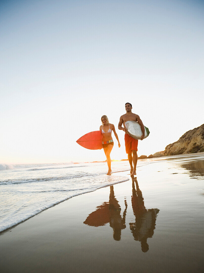 Couple walking on beach carrying surfboards, Newport Beach, CA, USA