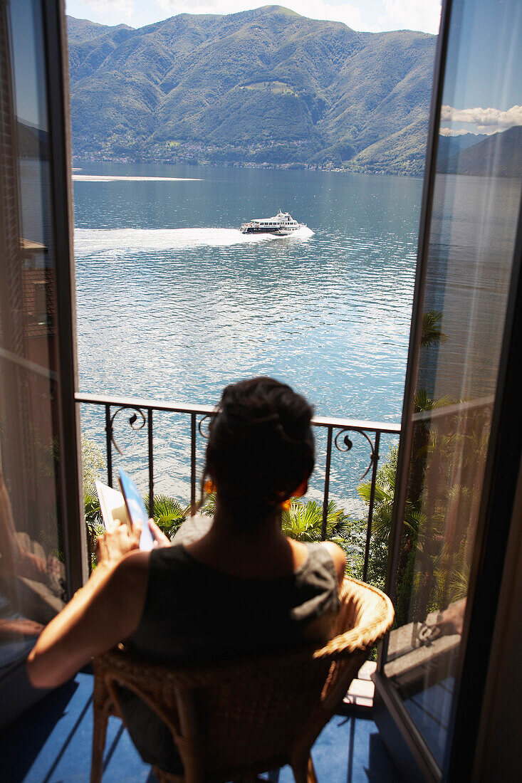 Italian woman sitting balcony looking at lake, Brissago, Lago Maggiore, Italy