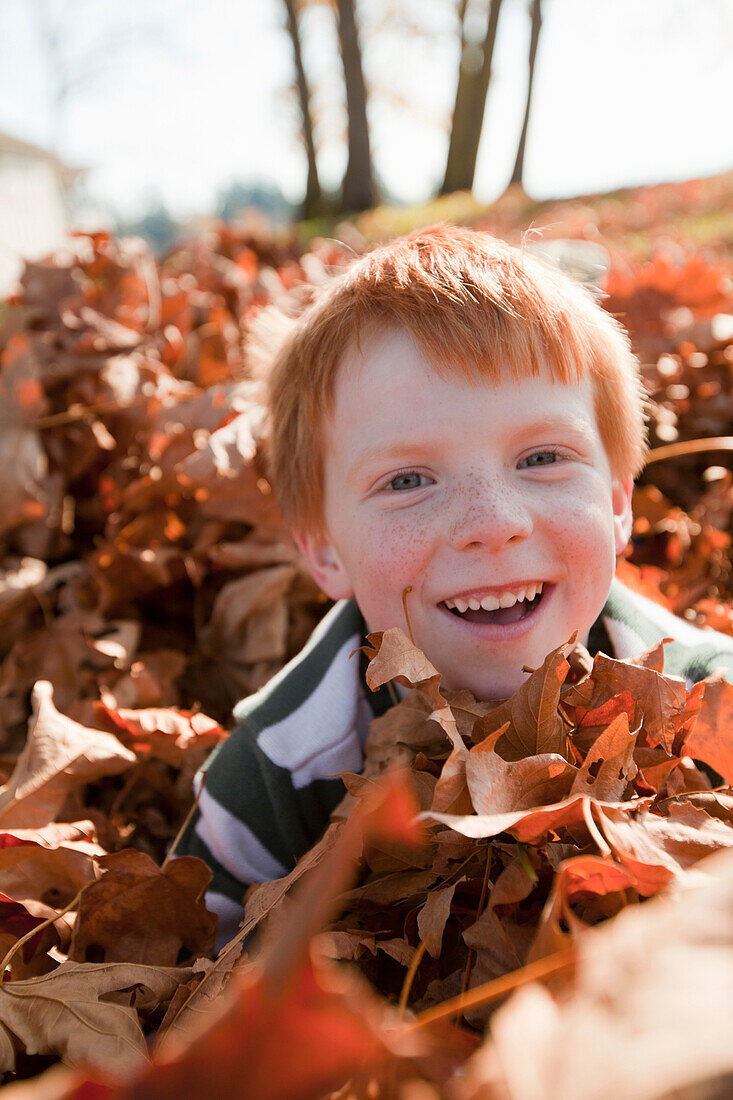 Caucasian boy playing in autumn leaves, Nanaimo, British Columbia, Canada